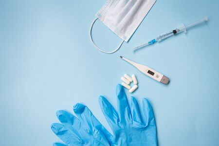Blue latex gloves on a blue background lie with pills, medical mask, thermometer and syringe. The concept of health and self-control for viruses and epidemics. Close-up.の写真素材