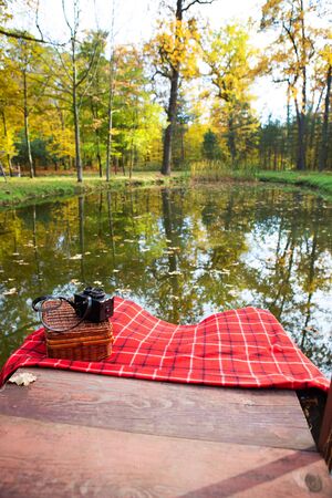 The old camera lies on a suitcase on a red plaid blanket. Wooden bridge near the lakeの写真素材