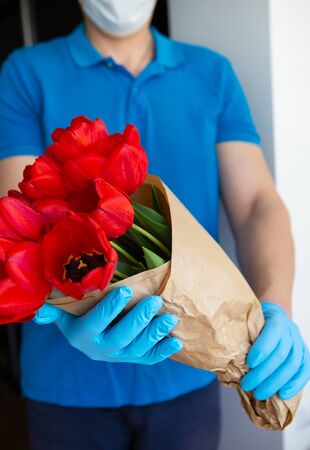 Contactless flower delivery by courier in a protective mask, medical gloves with a bouquet of red tulips. Close-up.の写真素材