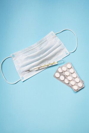 On a blue background are pills, a medical mask and a thermometer. Health and self-control concept for viruses and epidemics. Close-up. View from above.の写真素材