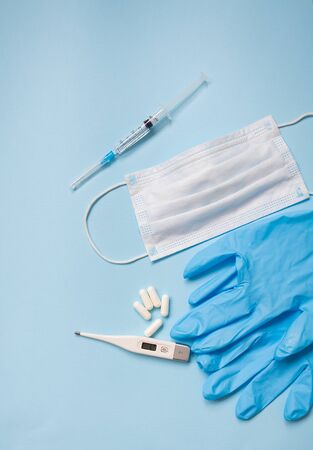 Blue latex gloves on a blue background lie with pills, medical mask, thermometer and syringe. The concept of health and self-control for viruses and epidemics.の写真素材