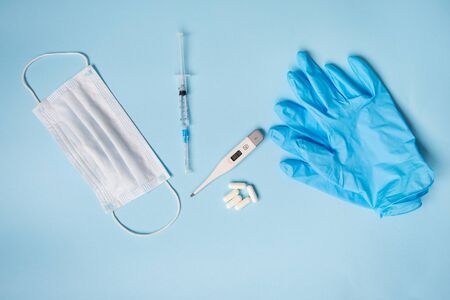 Blue latex gloves on a blue background lie with pills, medical mask, thermometer and syringe. The concept of health and self-control for viruses and epidemics. Close-up.の写真素材