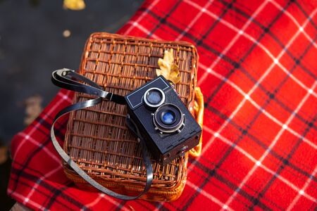 The old camera lies on a suitcase on a red plaid blanket. Wooden bridge near the lakeの写真素材