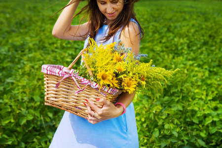 a girl in a blue board holds a basket of yellow flowers.の写真素材