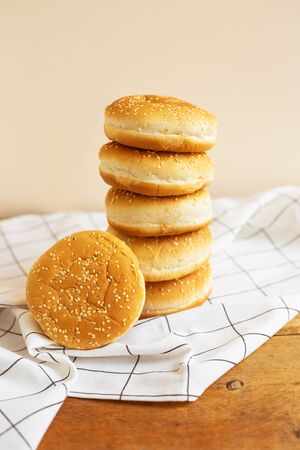 Freshly baked magnificent buns for hamburgers lie durg on each other in the form of a tower on a wooden table with a white checkered napkin. Close-upの写真素材