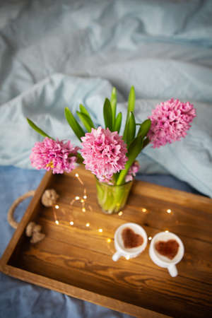 Beautiful bouquet of hyacinths. Two cups of cappuccino, a drawing of a heart on a foam on an old wooden tray. Surprise concept, beautiful morning, sunny day. Close-up. Garland, beautiful blinking.の写真素材