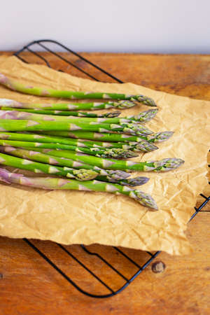 Fresh green asparagus spears wrapped in brown craft paper wrapper for healthy vegetarian cuisine lying on a wooden surface, top view. Close-upの写真素材