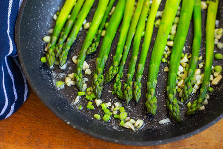 Tasty green asparagus is fried in a pan with garlic, next to it is a blue striped towel. Close-upの写真素材