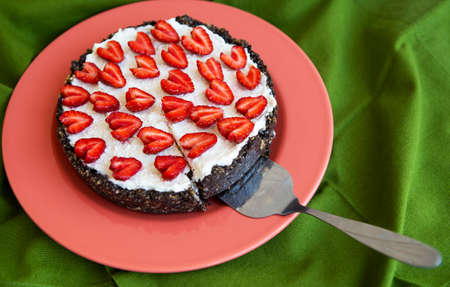 A strawberry cheesecake decorated with heart-shaped strawberries lies on a coral-colored plate, stands on a green napkin, cut off a slice. View from aboveの写真素材