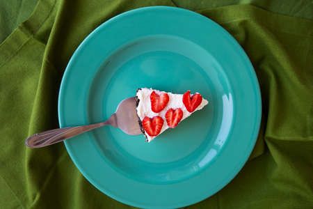 A piece of strawberry cheesecake decorated with heart-shaped strawberries lies on a mint-colored plate and stands on a green napkin. View from aboveの写真素材