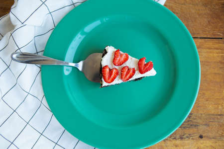 A piece of strawberry cheesecake decorated with heart-shaped strawberries lies on a mint-colored plate and stands on a checkered napkin. View from aboveの写真素材