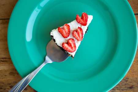 A piece of strawberry cheesecake decorated with heart-shaped strawberries lies on a mint-colored plate and stands on a checkered napkin. View from aboveの写真素材