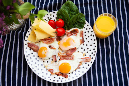 Fine breakfast, on a plate fried eggs with bacon, slices of cheese, spinach, cherry tomatoes with a glass of fresh orange juice.の写真素材