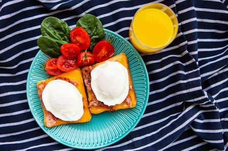 Poached egg on toasted English toast with spinach, cherry tomatoes, orange juice, striped napkin.の写真素材