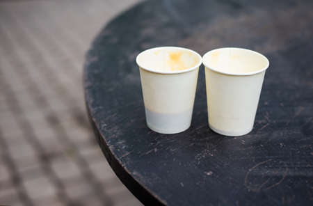 Two plastic glasses with coffee stand on the street on a wooden table. Close-up