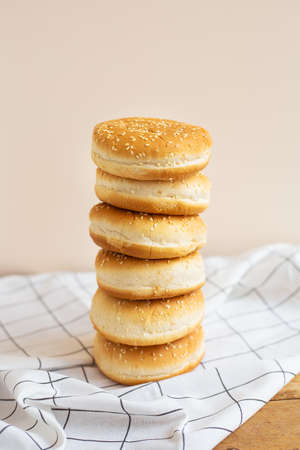 Freshly baked magnificent buns for hamburgers lie durg on each other in the form of a tower on a wooden table with a white checkered napkin. Close-upの写真素材