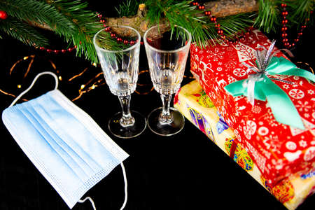 Christmas background with fir branches, two champagne glasses, gift, medical mask, concept of New Year's decorの写真素材