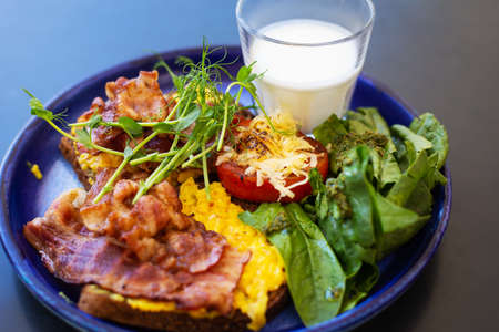 Very bright and healthy breakfast on a plate - bacon, egg, salad, tomato, cheese, a glass of yogurt. Close-upの写真素材