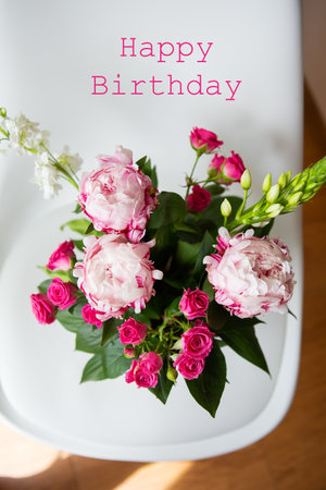 A beautiful bouquet of tender pink peonies and small roses stands on a white chair. Wedding bouquet, birthday. Happy birthday letteringの写真素材