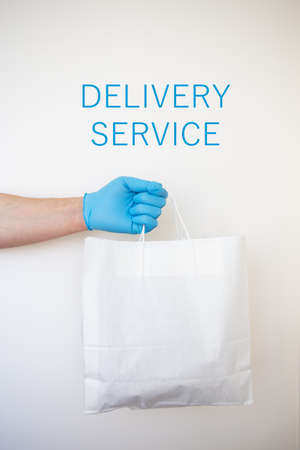 Contactless home shopping delivery with gloves holding a paper bag with food isolated on white background. The concept of quarantine and isolation during the coronavirus pandemic.の写真素材