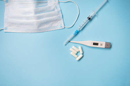 On a blue background are pills, a medical mask, a thermometer and a syringe. The concept of health and self-control for viruses and epidemics. View from above.の写真素材