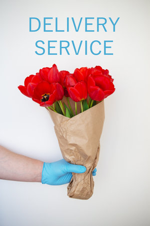 Contactless delivery of disposable gloves of a bouquet of red tulips, the concept of quarantine and isolation during the coronavirus pandemic and the economic downturn of flower enterprisesの写真素材