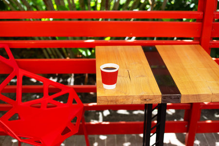 A wooden table on which there is a red plastic cup with coffee. Summer beautiful terrace in greenery. Cozy placeの写真素材