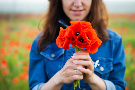 A young girl holds a bouquet of beautiful red poppies in her hand in front of her. Close-upの写真素材