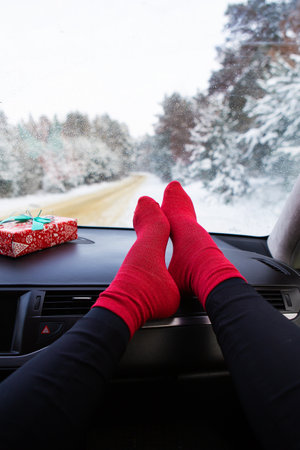 The legs of a girl in red socks sits in the car in the winter, against the background of a winter...