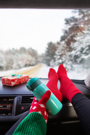 The girl is holding a flask while sitting in the car in winter, on the background of the winter forest. Travel, trip and winter conceptの写真素材