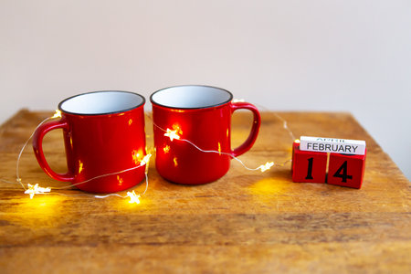 Two cups of coffee in red cups on a background of garlands. Postcard with date and month. Morning...