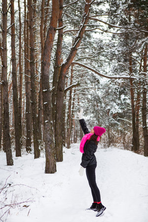 A girl in a pink scarf and hat stands in the middle of a pine forest. Beautiful pine forest on a frosty dayの写真素材