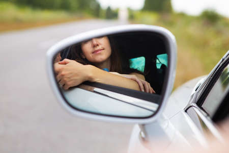 A young girl driving a car, the girl looks in the side mirror. Delivery for the right to drive a carの写真素材