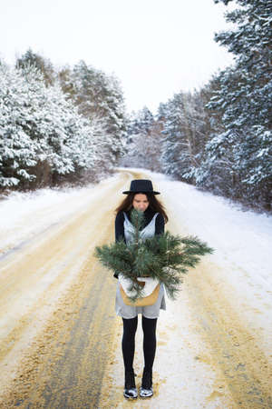 A young girl in a silver dress and hat stands with her back in the middle of a beautiful winter road in the forestの写真素材