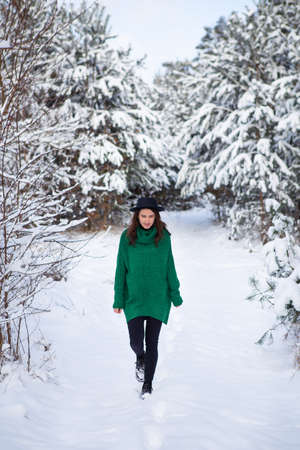 A young girl in a dark green sweater and hat stands in the middle of a beautiful winter forestの写真素材