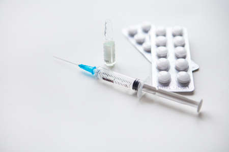 Preparation for vaccination against covid-19. Syringe, vaccine, pills, medical mask on a white tableの写真素材