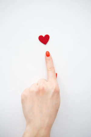 The girl points with her hand to a small red heart. The concept of care and loveの写真素材