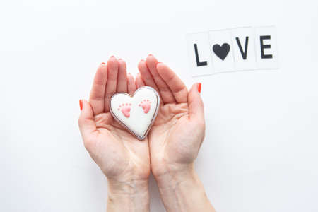 Beautiful children's footprint in the shape of a heart, the girl's hands hug the heart. Love letteringの写真素材