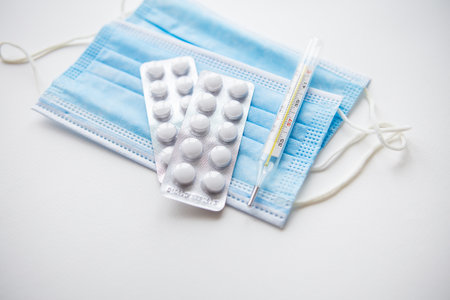 Preparation for vaccination against virus. Thermometer, pills, medical mask on a white table. View...