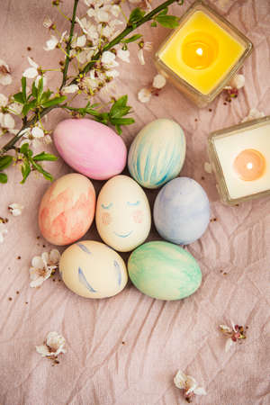 Beautiful watercolor paints on Easter eggs that lie on a delicate pink cloth along with burning candles. Easter conceptの写真素材