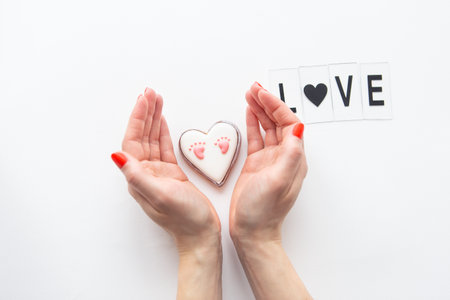 Beautiful children's footprint in the shape of a heart, the girl's hands hug the heart. Love letteringの写真素材