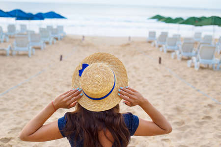 Beautiful girl in a hat sits with her back on a sandy beach.の写真素材