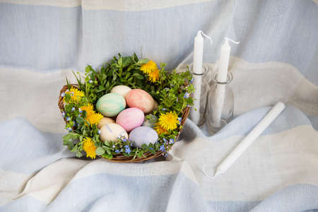 A beautiful spring bouquet in a wooden basket with Easter eggs painted with watercolors. White candles lie nearbyの写真素材