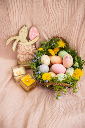 On a pastel bedspread is a basket of grass and various bright flowers, a rabbit. The basket contains Easter eggs painted with watercolors in beautiful pastel colorsの写真素材