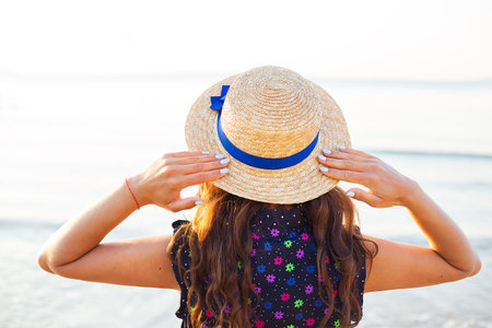 Beautiful girl in a hat stands with her back on a sandy beach.の写真素材