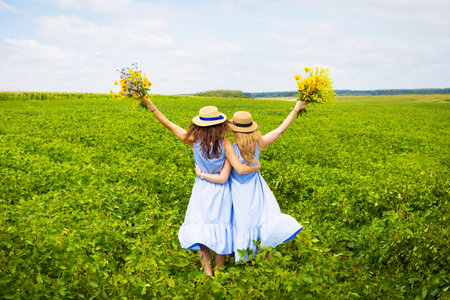 Two beautiful girlfriends in hats hugging in green field.の写真素材