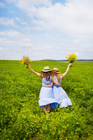 Two beautiful girlfriends in hats hugging in green field.の写真素材