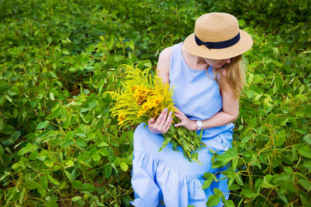 Girl in a green field sits with a bouquet of wild flowers.の写真素材
