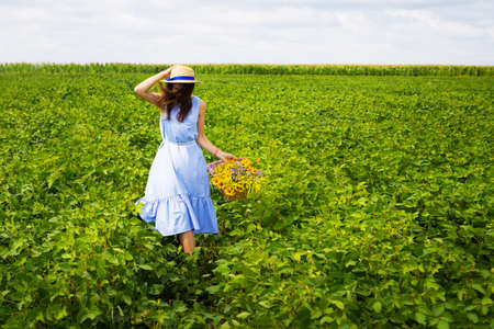 Young beautiful woman looks at the setting sun and holds a straw hat, sits on a large pile of straw balesの写真素材