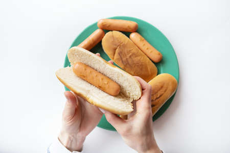 Fresh buns for making hot dogs that lie on a green plate along with sausages that the girl holds in her hands. Top view, close-upの写真素材